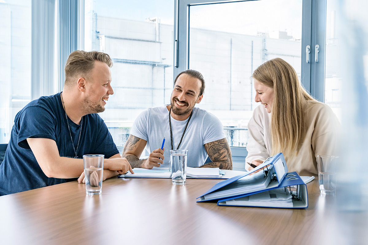 Drei Kollegen sitzen an einem Schreibtisch und arbeiten zusammen.