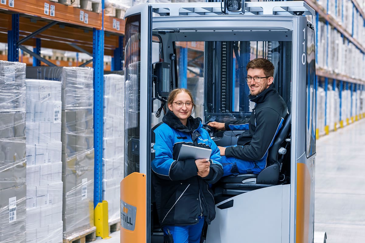 Zwei Kollegen arbeiten im Lager, einer sitzt auf dem Gabelstapler.